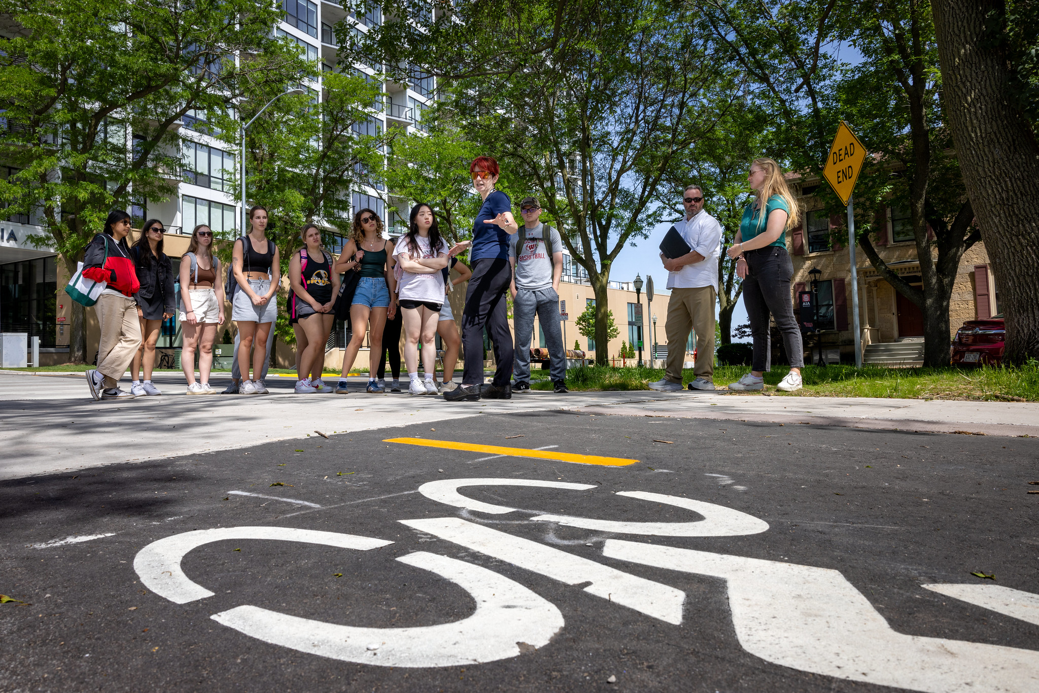 A group of people are standing outside by a road in the city of Madison