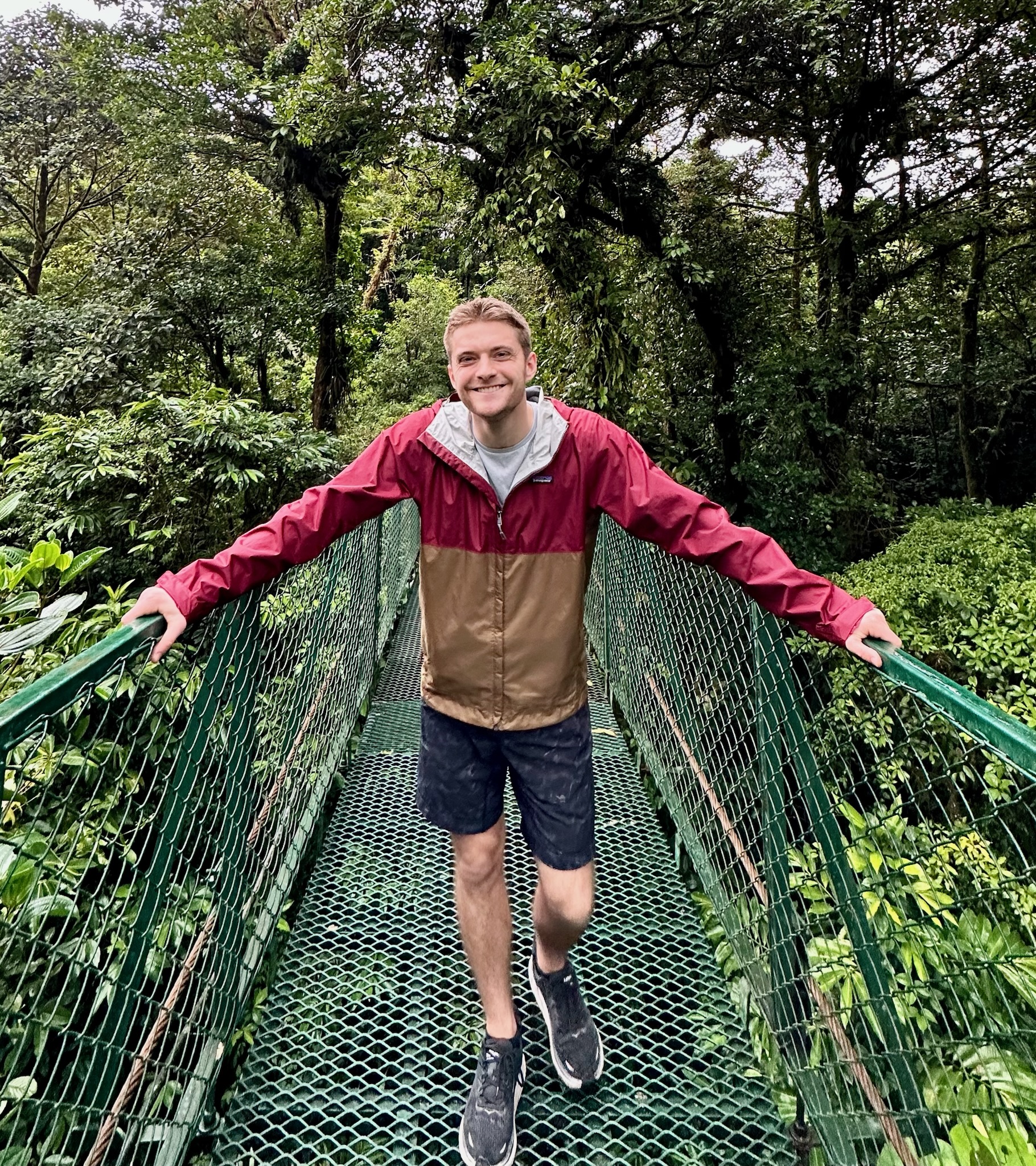 A student stands in the middle of a suspended bridge in a rainforest