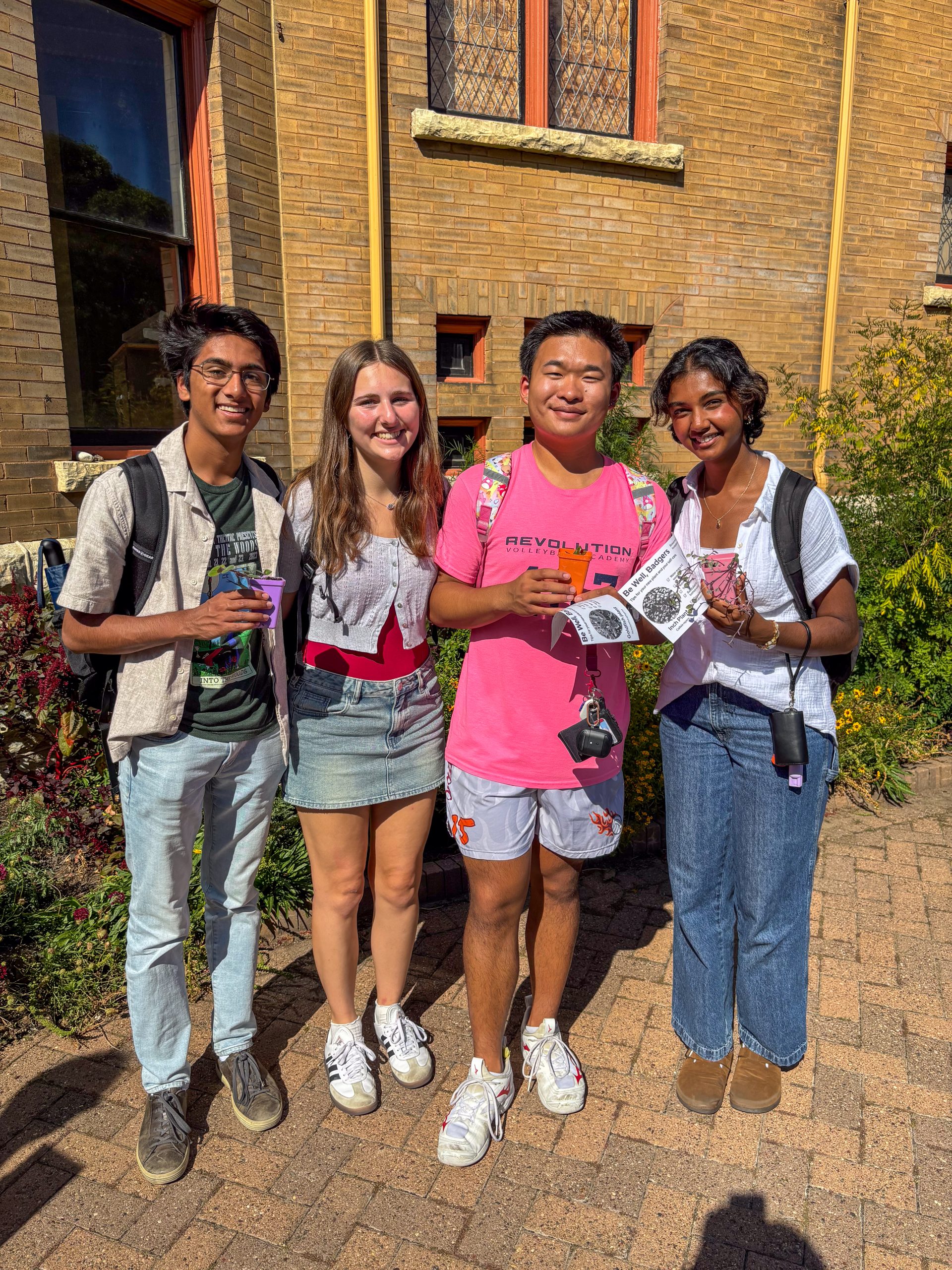 Four students are standing next to each other outside and smiling at the camera
