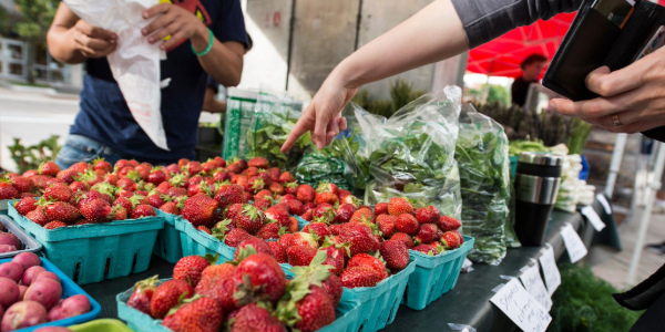 A person attending a farmers' market points to strawberries
