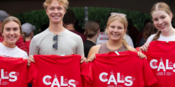 Four students pose for a photo and smile as they hold up CALS shirts