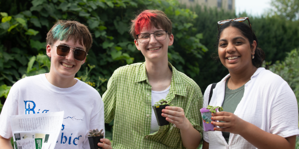 Three students smile at the camera, they each are holding a small potted plant